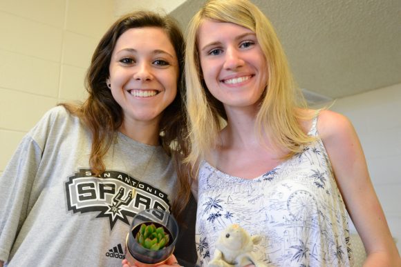 Two young women holding a small plant and a small stuffed animal