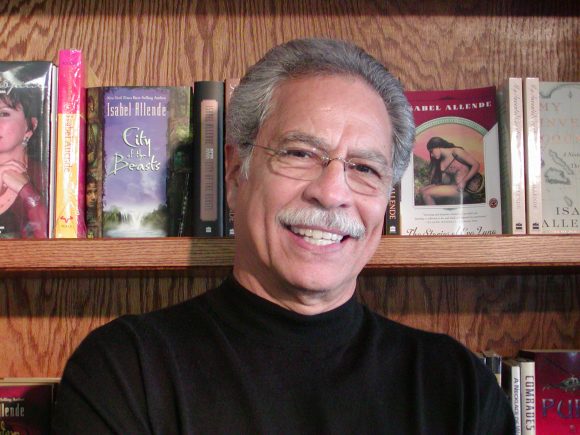 Smiling man with mustache in front of bookshelf.