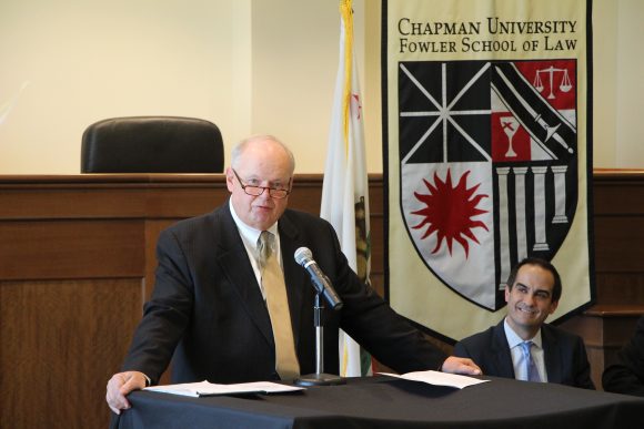 man speaking into microphone as another man looks on from behind