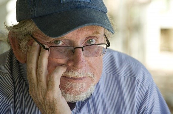 man wearing baseball cap and glasses with hand on face - looking at camera