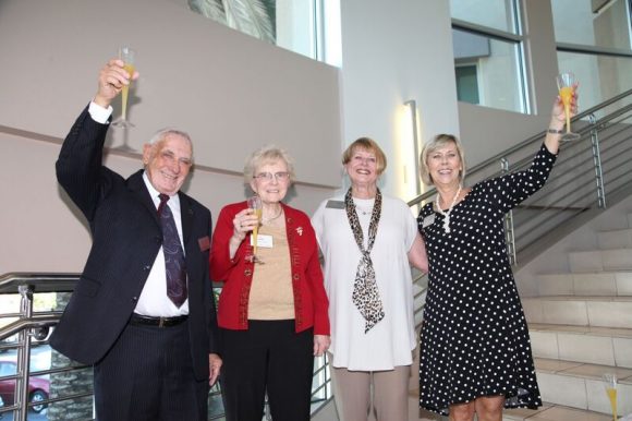 one man and three women - holding champagne classes up for a toast and smiling