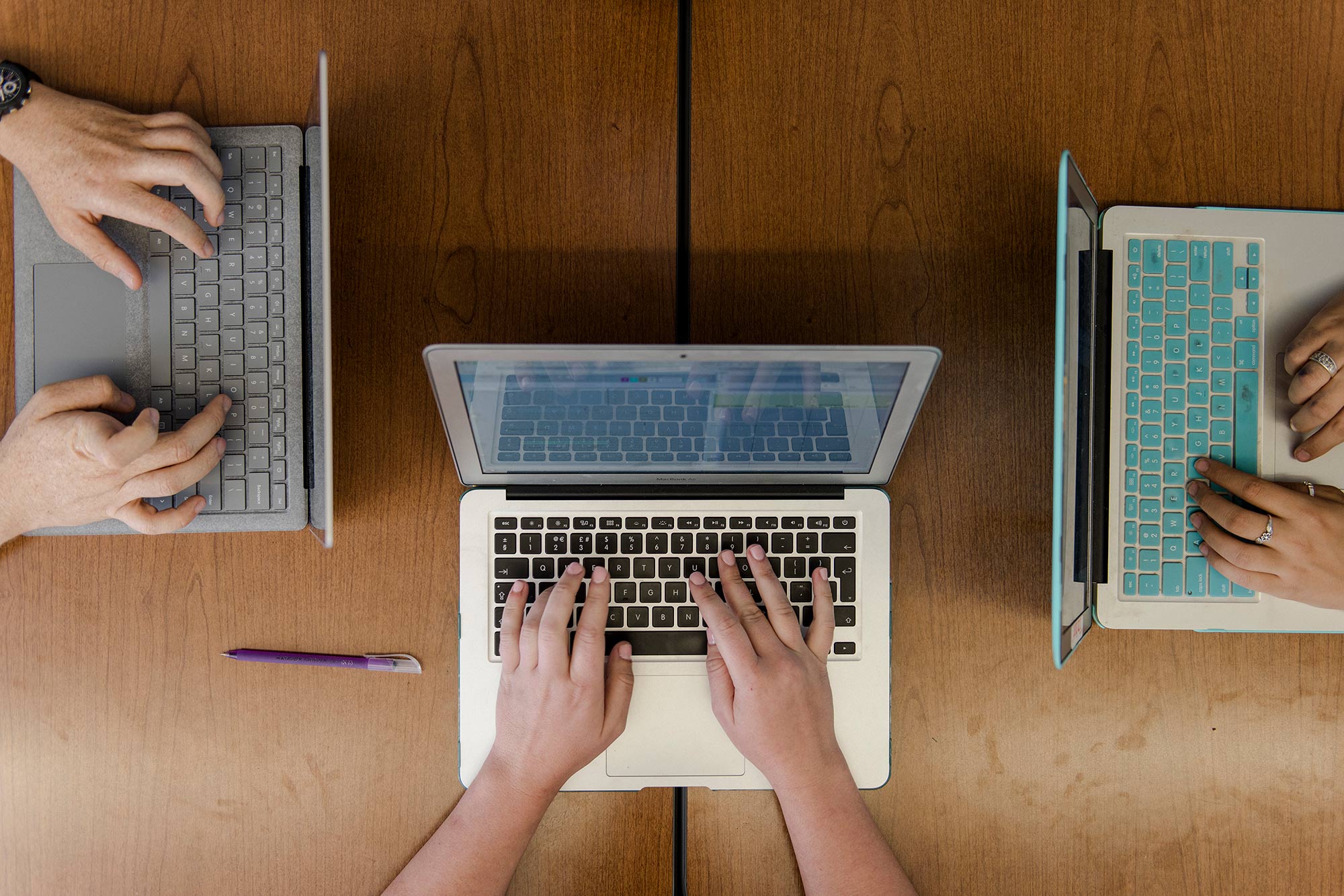 Three laptops in use. Only hands and computers visible.