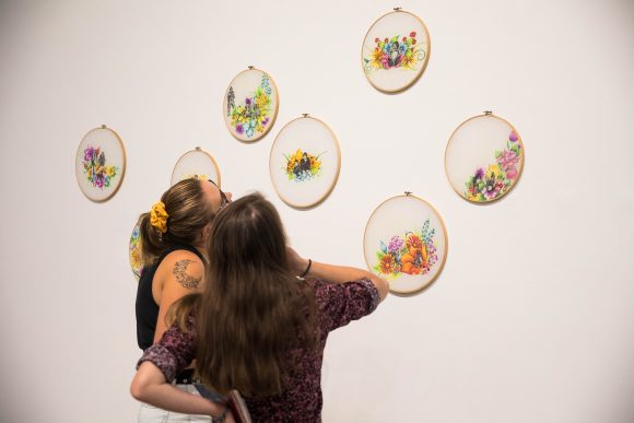 Women look at embroidery hoop artworks. 