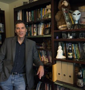 Chris Bader smiles in front of his bookshelf