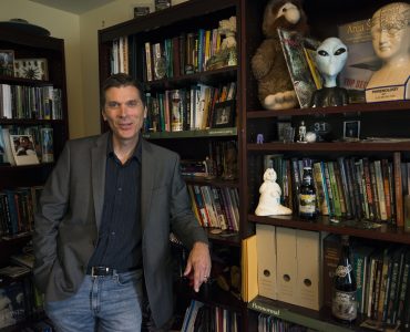 Chris Bader smiles in front of his bookshelf