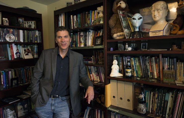 Chris Bader smiles in front of his bookshelf