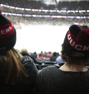 the heads of two people in knitted beanies watching a hockey game