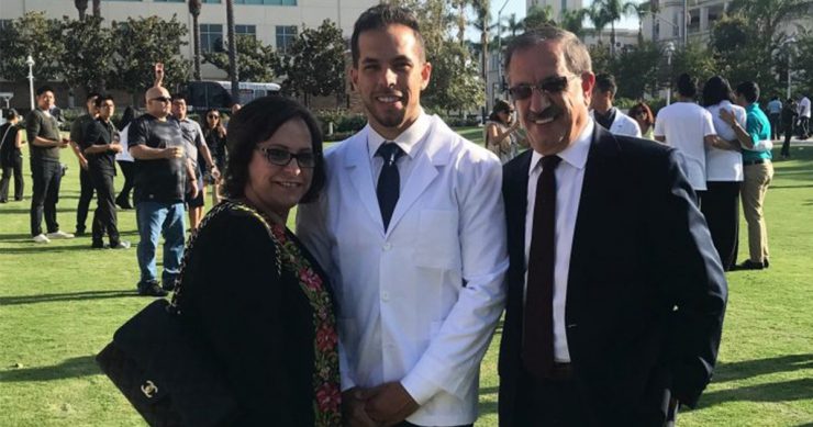 ramsey halim in a white pharmacist coat with his mom and dad to his left and right standing in grass with chapman university buildings behind them.