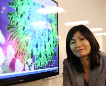 Pharmacy professor Jerika Lam poses next to a screen image of a virus molecule.