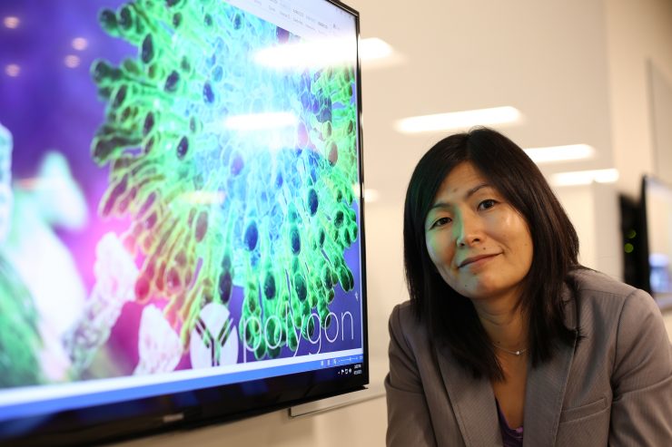 Pharmacy professor Jerika Lam poses next to a screen image of a virus molecule.