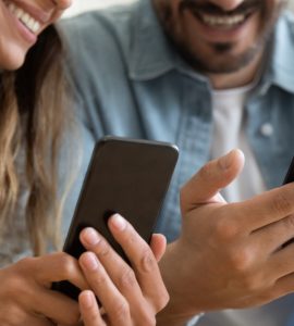 Couple smiling while looking at phones.
