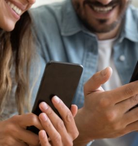 Couple smiling while looking at phones.