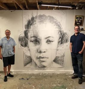 Artist and Hilbert founder pictured standing on opposite ends of large portrait of woman.