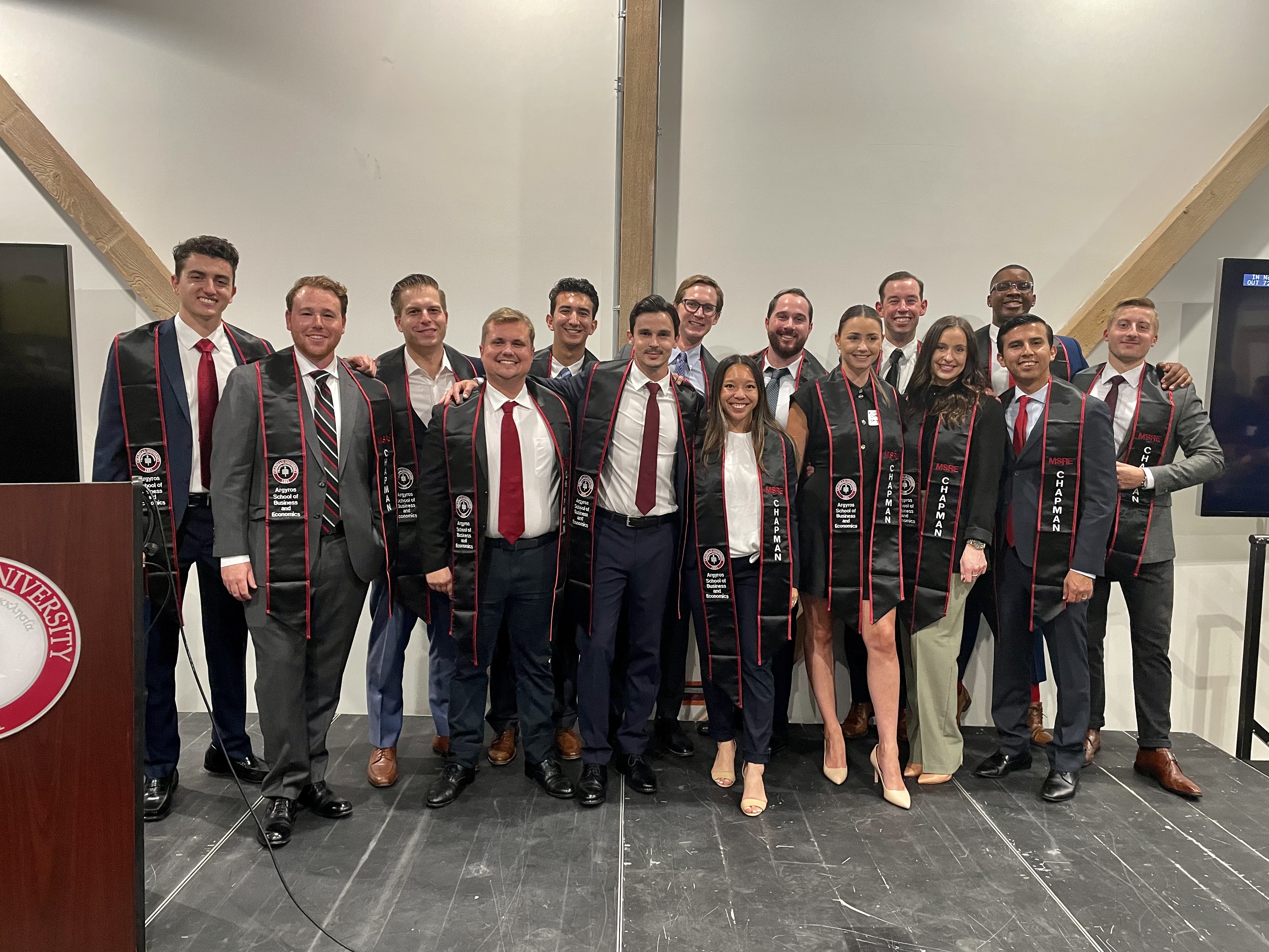 group of students on a stage wearing academic hoods