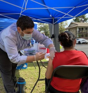 Medical personel gives a COVID-19 vaccination to an anonymous woman in an outdoor booth.