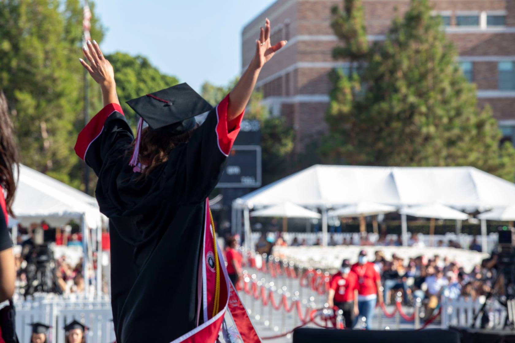 woman in black cap and gown with arms raised as she crosses the stage