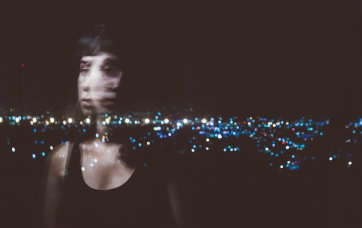 Blurred reflection of woman as she gazes gazes at city lights.