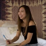 college student sitting on dorm bed with notebook