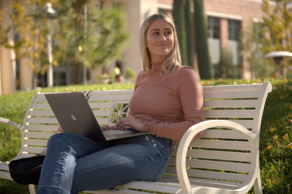 smiling woman sitting on outdoor bench with computer