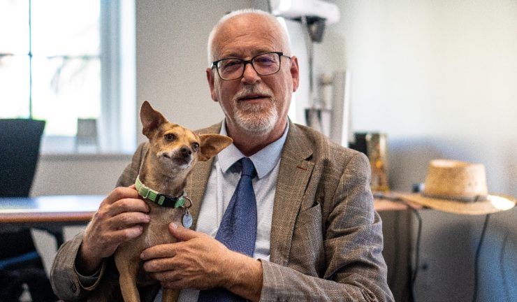 Photo of School of Comm Dean M. Andrew Moshier in university office with pet dog.