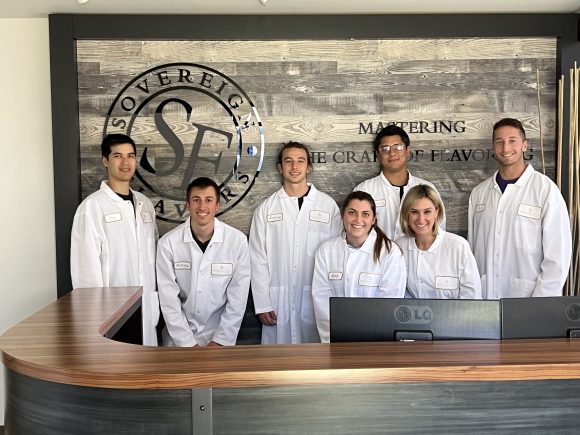 seven adults in lab coats in front of sovereign flavors sign