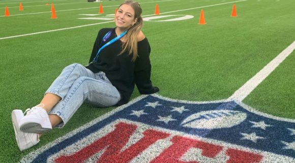 Sydney Legrett poses with NFL symbol on football field