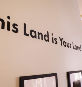 Wall displayed with art exhibition title This Land is Your Land.