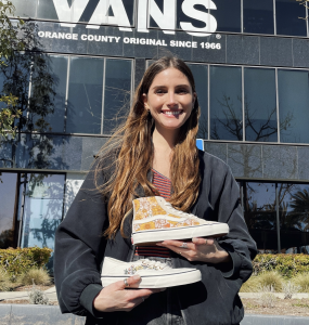 Lizann Stauber standing in front of Vans holding the two shoes she designed.