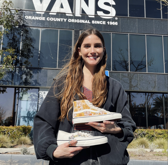 Lizann Stauber standing in front of Vans holding the two shoes she designed.