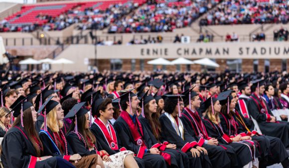 rows of graduates in caps and gowns on seats in ernie chapman stadium