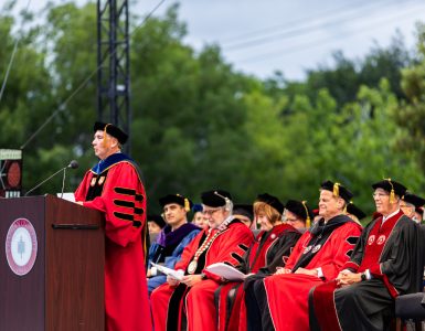 administrators in red academic robes on commencement platform
