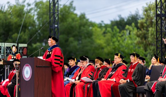 administrators in red academic robes on commencement platform