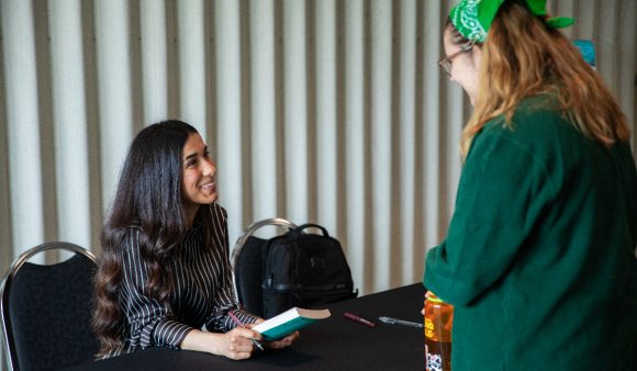 nadia murad sitting at table smiling at standing student