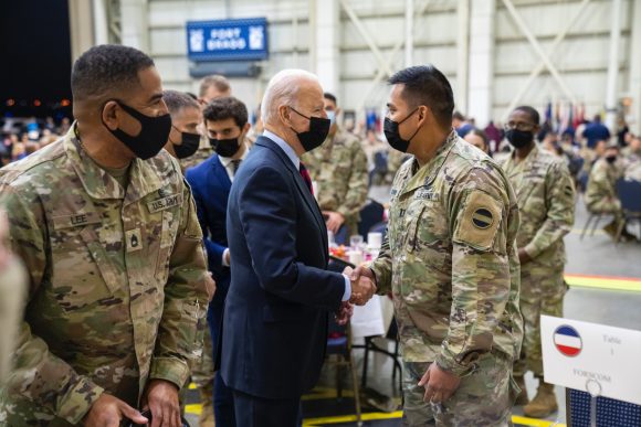 mitchell rosenberg looks over the shoulder of joe biden who is shaking hands with soldiers at fort bragg