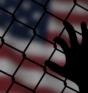 a hand grasps at a chain link fence with the American flag in the background