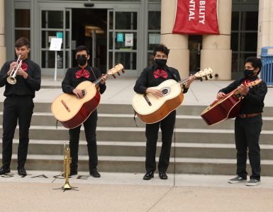 four musicians playing mariachi instruments in front of library