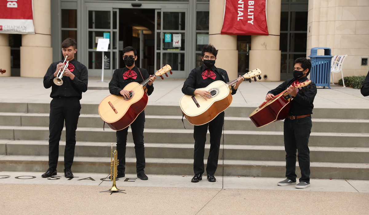four musicians playing mariachi instruments in front of library