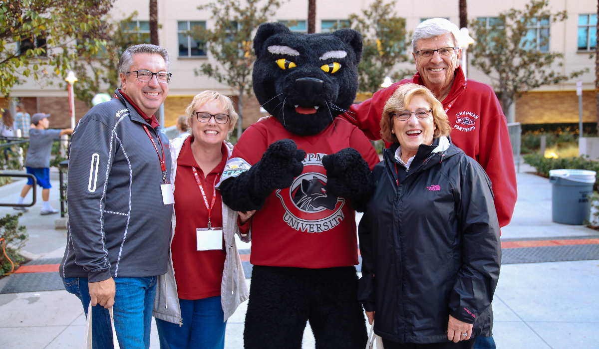 Pete the Panther mascot stands with two men and two women in Chapman gear on Chapman campus