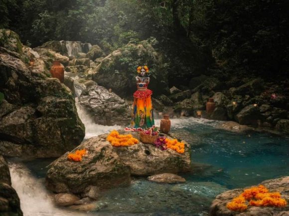Woman in Dia de los Muertos costume stands with marigolds by water