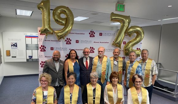 daniele strip-a stands with group of alumni in yellow stoles and balloons spelling out 1972