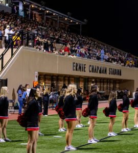 cheerleaders stand on field in front of packed stadium stands