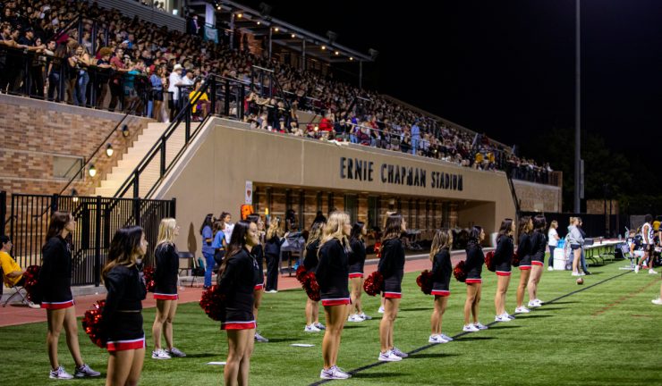 cheerleaders stand on field in front of packed stadium stands