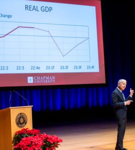 Dr. Jim Doti pointing his finger at a large screen displaying a graph explaining "Real GDP"
