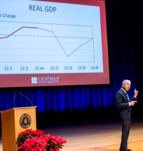 Dr. Jim Doti pointing his finger at a large screen displaying a graph explaining "Real GDP"
