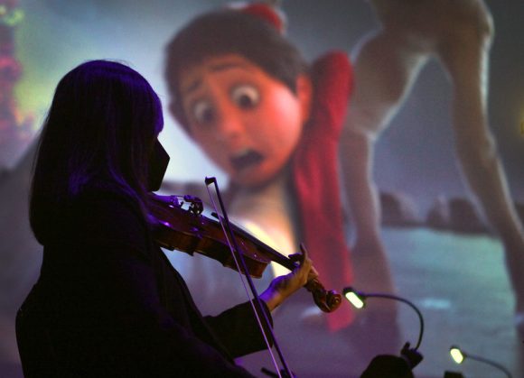 violinist silhouetted against screen with scene from Coco