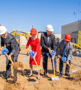 Four nicely dressed people in suits and hardhats digging into the ground of a construction site