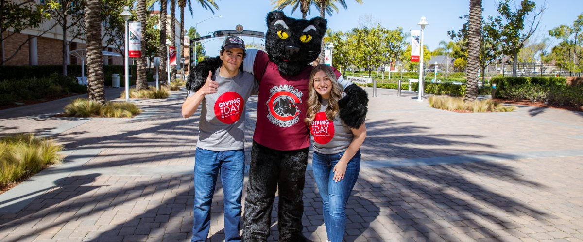 Jacob Zamore and Rachel Bern pose with Pete the Panther in front of Schmid Gate on Chapman campus