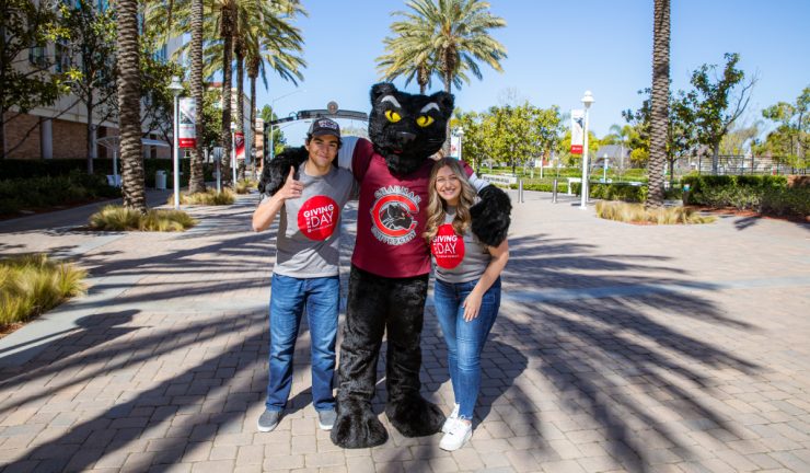 Jacob Zamore and Rachel Bern pose with Pete the Panther in front of Schmid Gate on Chapman campus