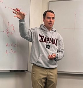 john howell in chapman sweatshirt gesturing at whiteboards in classroom