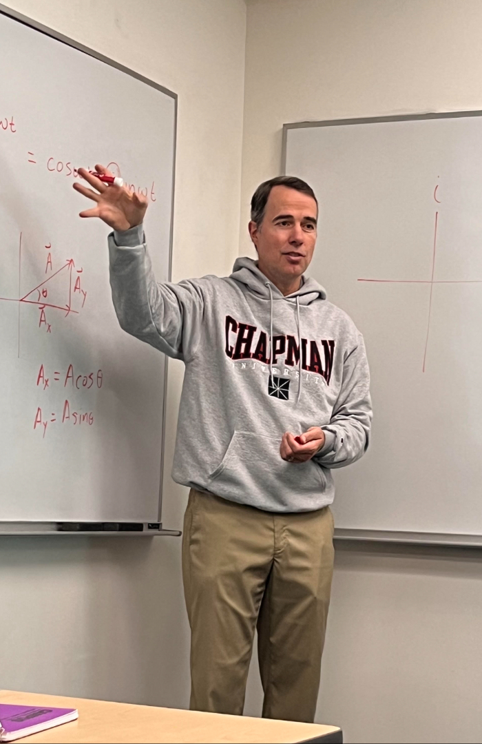 john howell in chapman sweatshirt gesturing at whiteboards in classroom